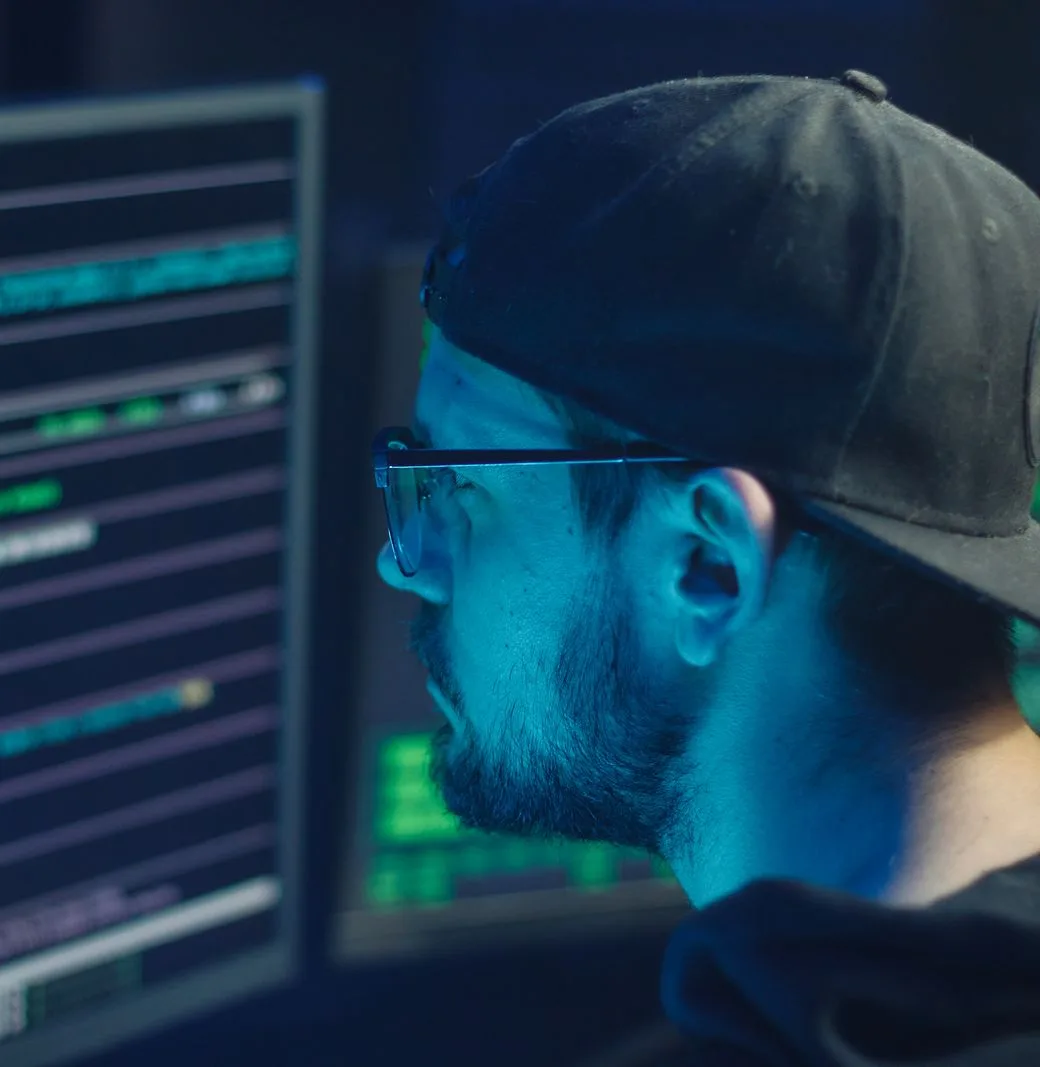 Penetration tester reviewing terminal output across two monitors in a dark office
